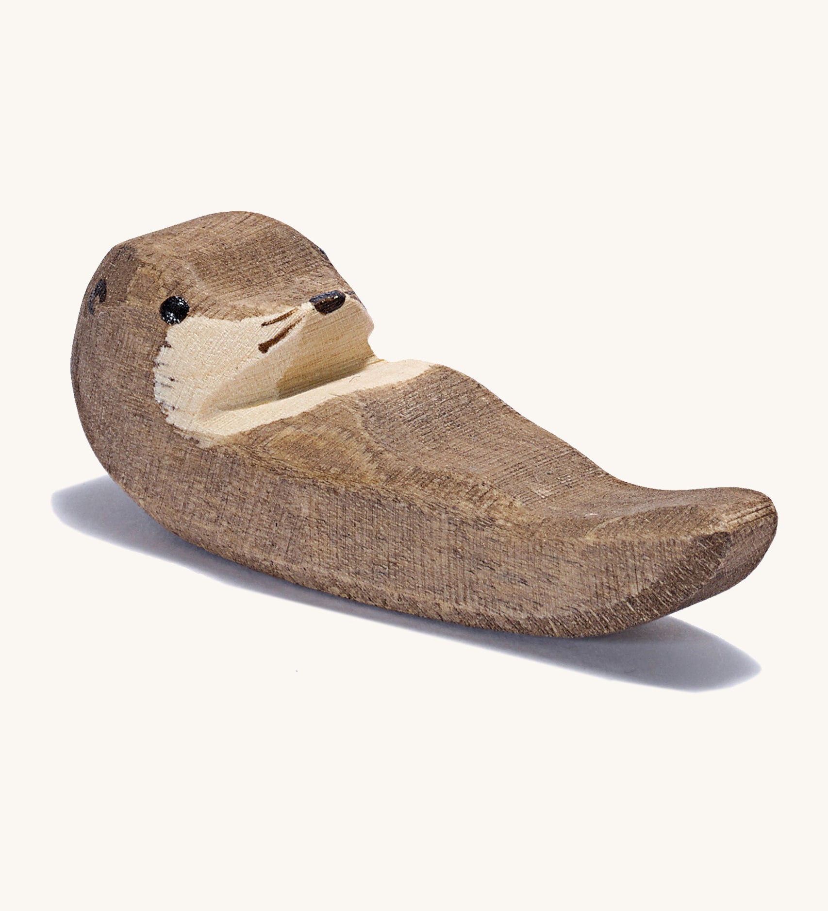 A small wooden Ostheimer swimming otter figure on a cream background.