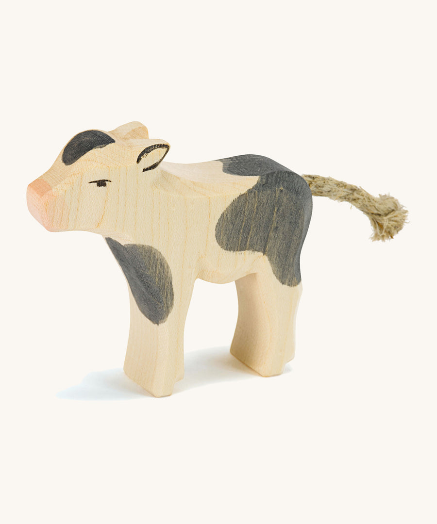 A wooden black and white Ostheimer standing cow figure on a cream background.