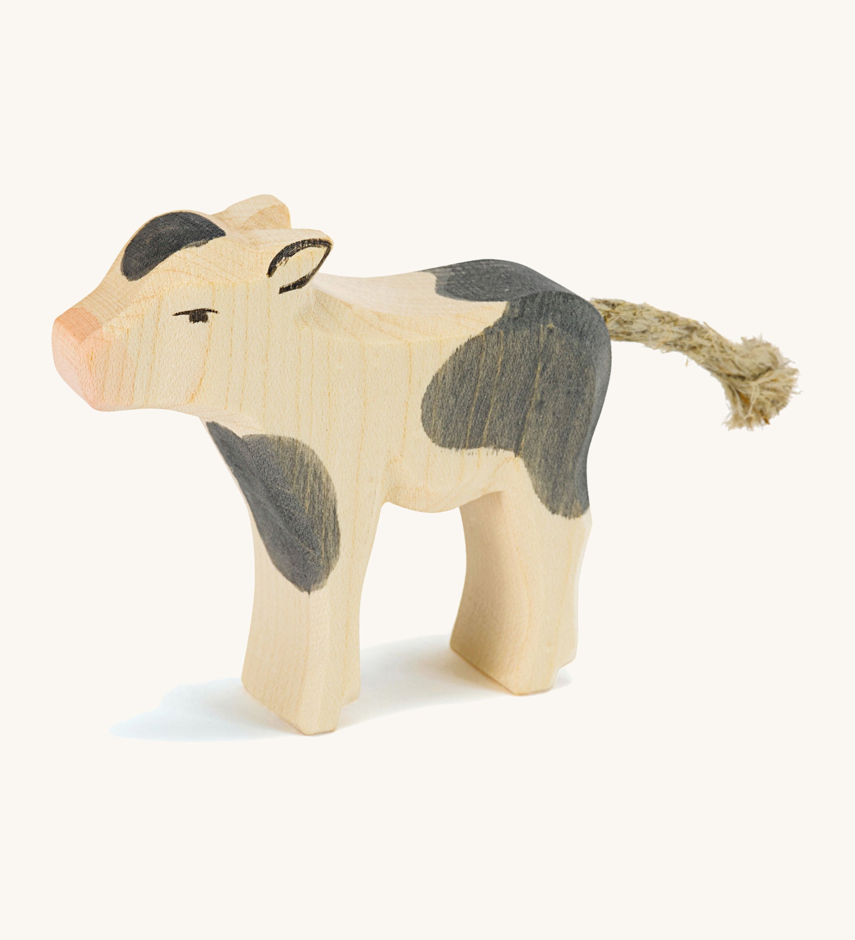 A wooden black and white Ostheimer standing cow figure on a cream background.