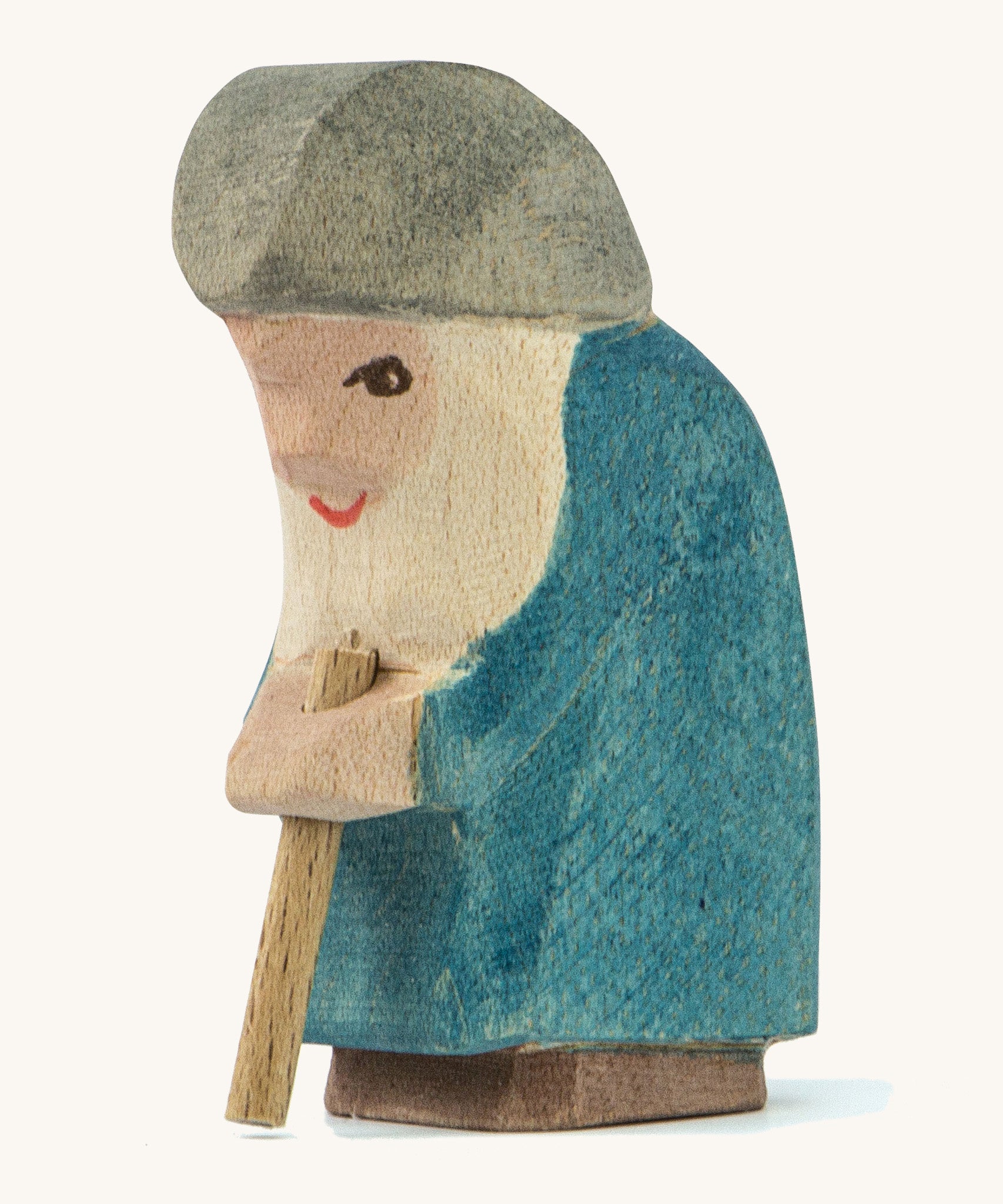 A wooden Ostheimer Willi dwarf figure wearing a blue coat and a grey hat holding a wooden staff on a cream background.