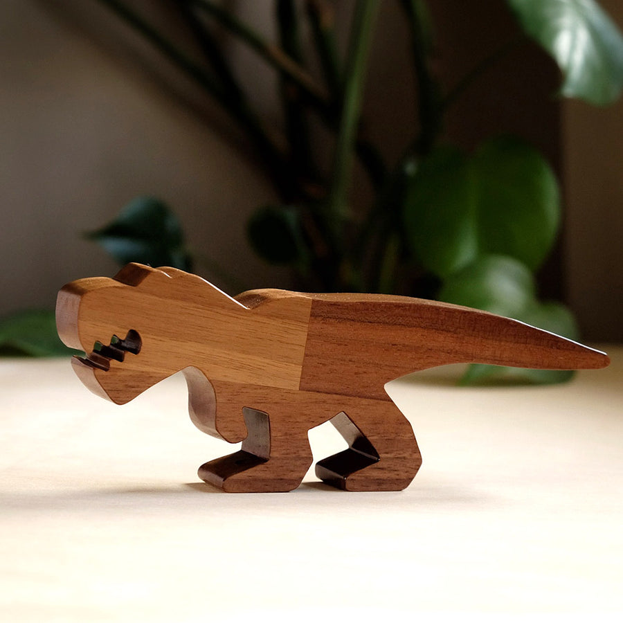 Close up of O-WOW sustainable Walnut T-Rex dinosaur toy on a white floor in front of some green plants