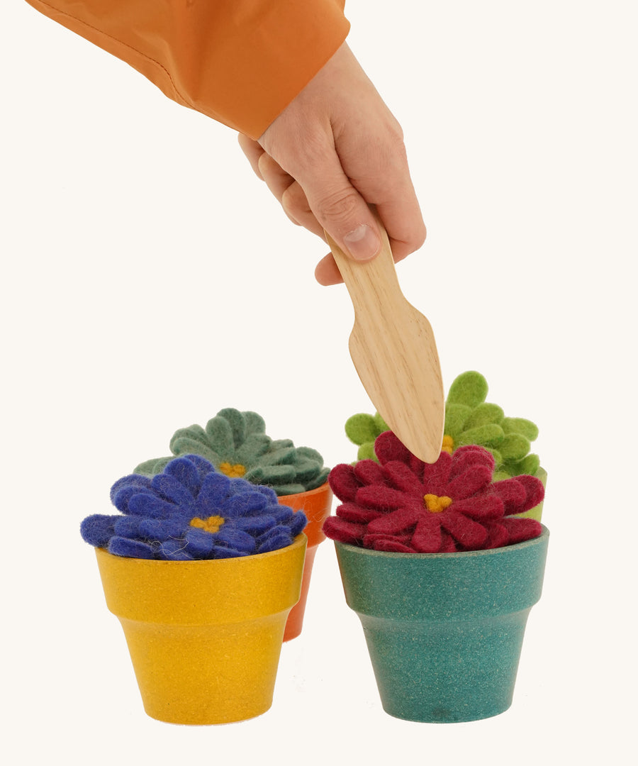 4 felted aster flowers in multicoloured plan pots with a hand holding a gardening tool above