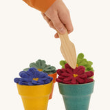 4 felted aster flowers in multicoloured plan pots with a hand holding a gardening tool above