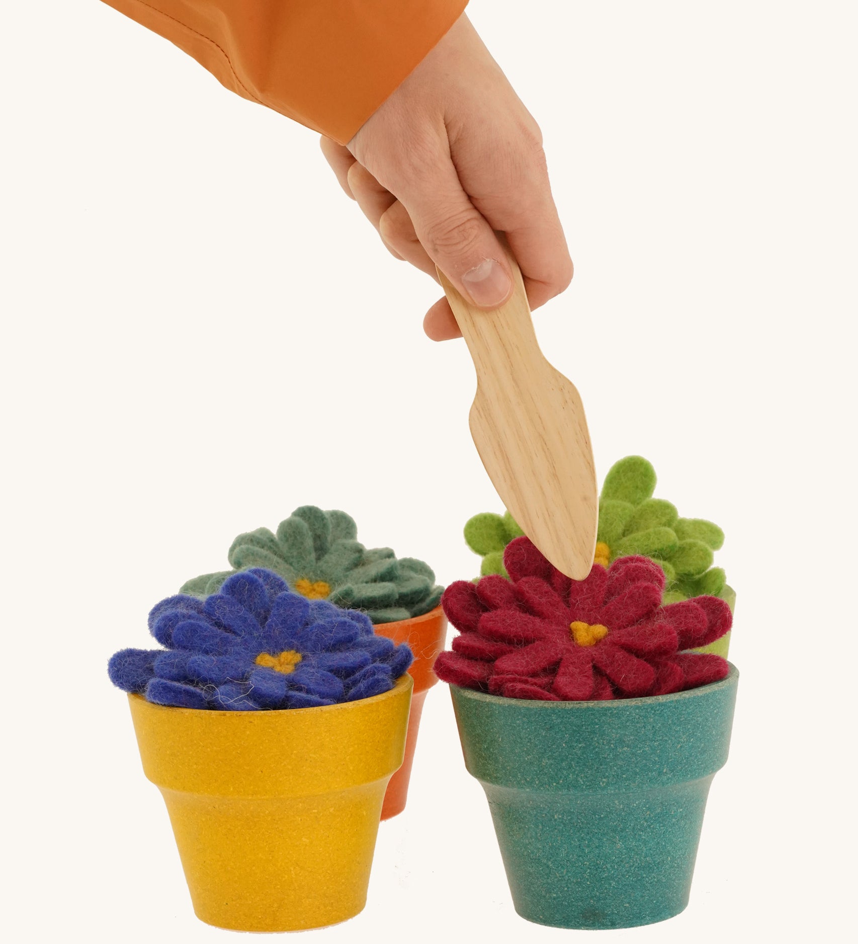 4 felted aster flowers in multicoloured plan pots with a hand holding a gardening tool above