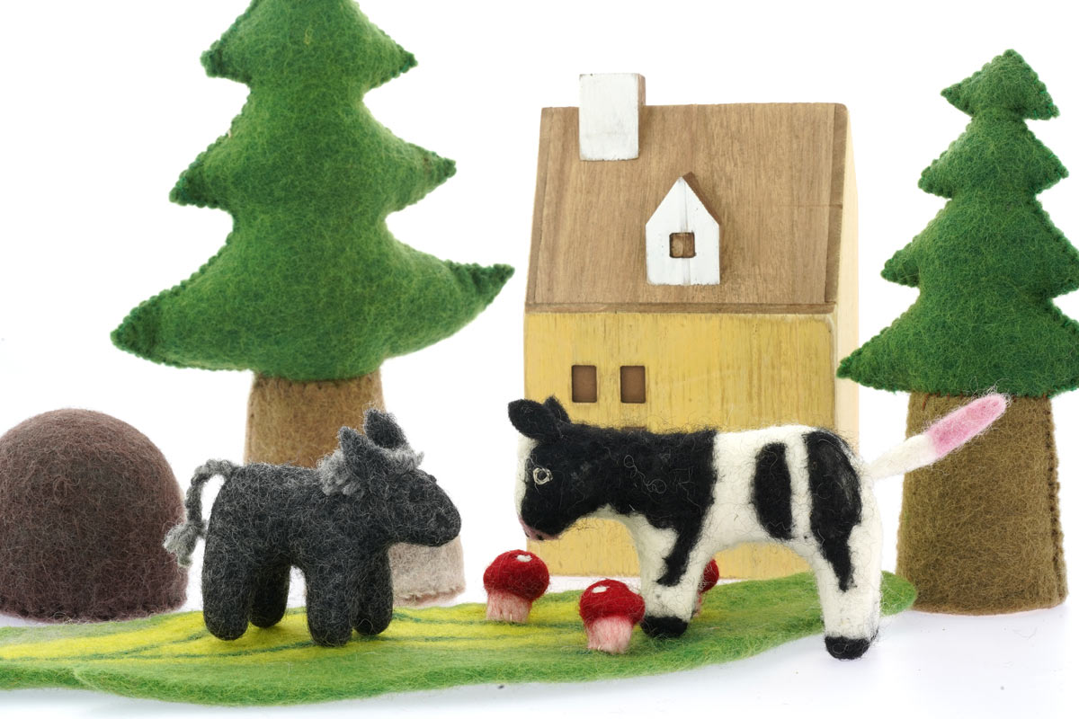 Close up of the Papoose soft felt donkey and cow toys on a Papoose play mat in front of a small wooden house