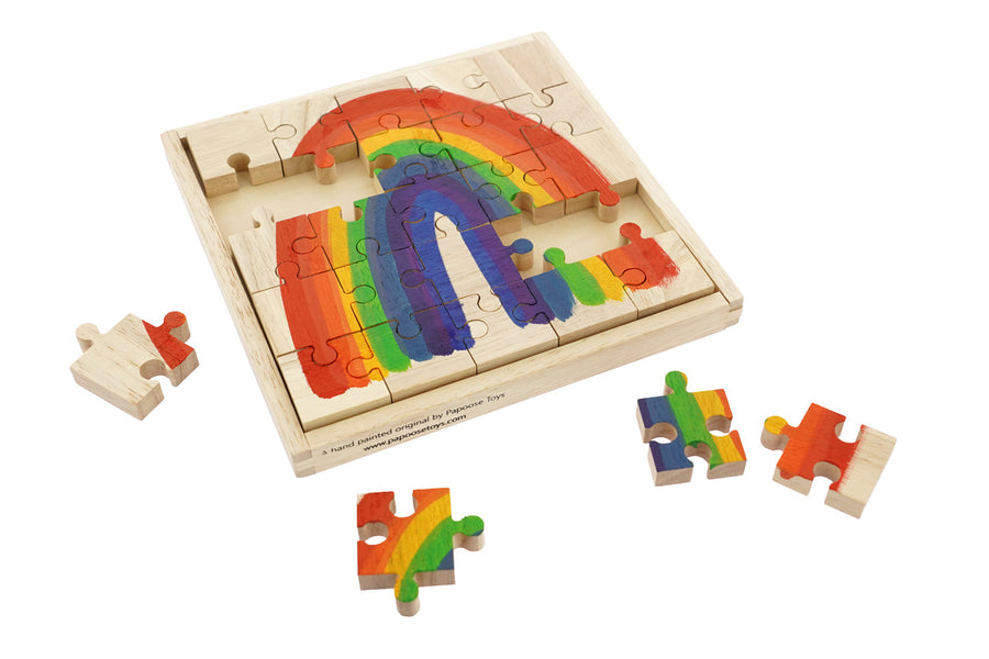 Pieces of the Papoose plastic-free wooden rainbow jigsaw scattered around the wooden base on a white background