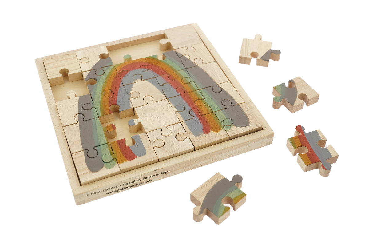 Pieces of the Papoose childrens earth rainbow jigsaw puzzle scattered around the wooden base on a white background