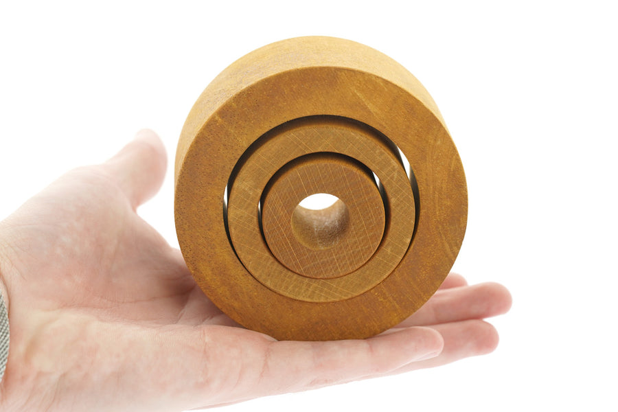 Close up of a hand holding the Papoose wooden Waldorf nesting tubes on a white background