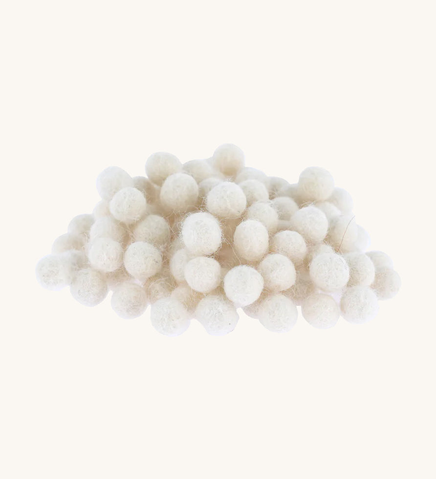 white felted pom poms piled up on a cream backround