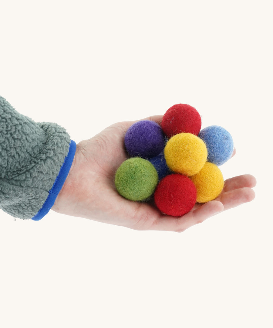 Felted rainbow balls in a hand on a cream background