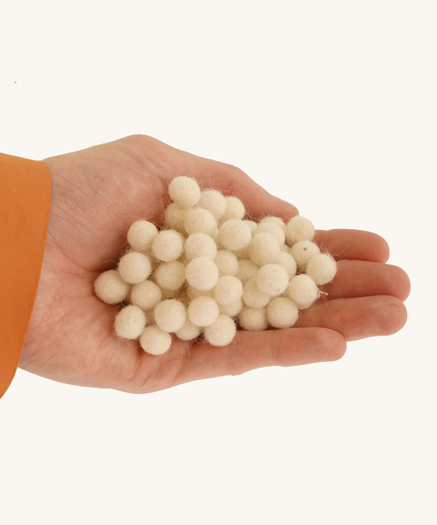 A close up of the felted pom poms in a hand on a cream background