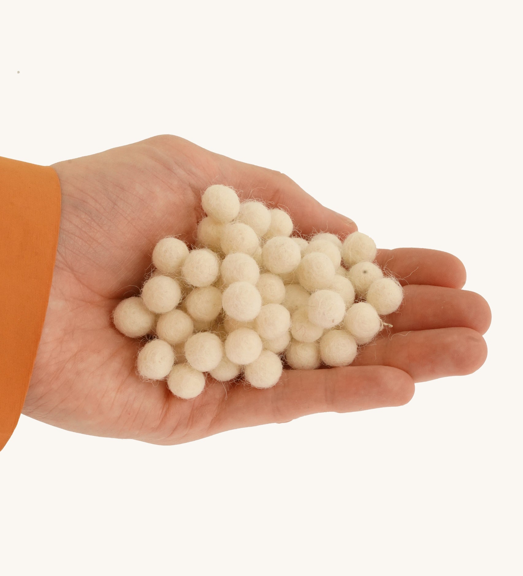 A close up of the felted pom poms in a hand on a cream background