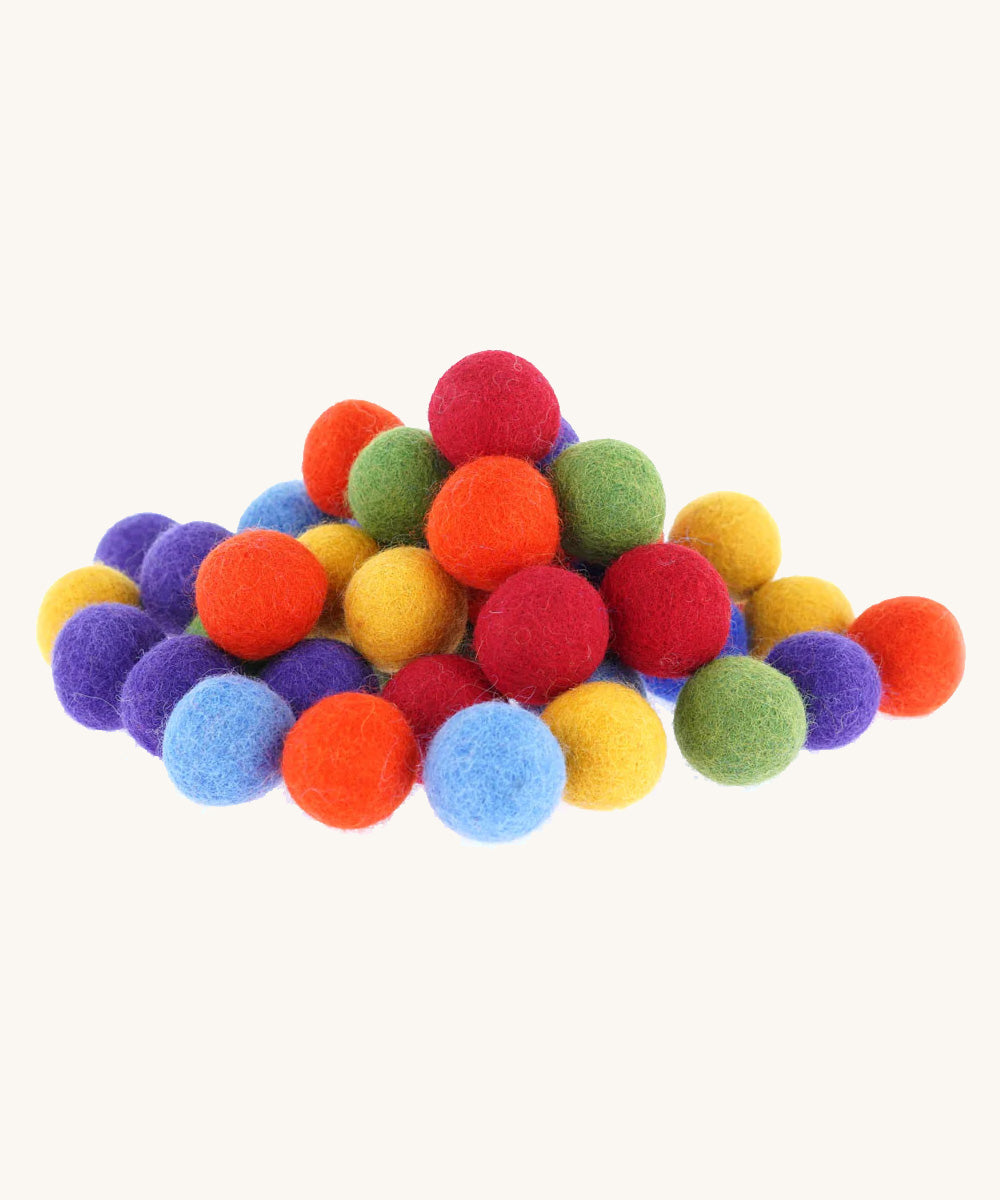 A stack of felted rainbow pom pom balls on a cream background