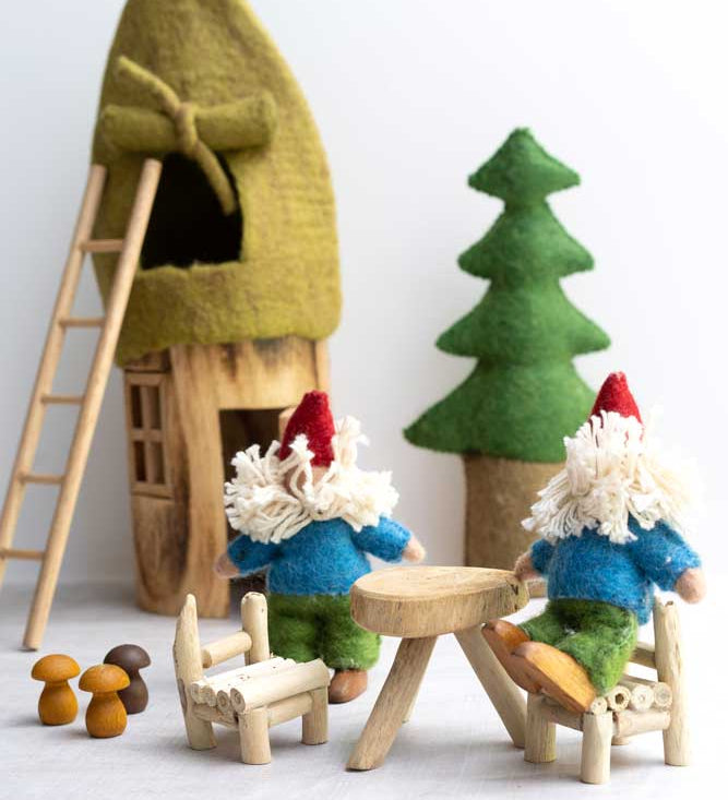 Two Papoose Toys Bearded Felt Tomten Gnome's sat at a wooden table and chairs with a felt Gnome house and pine tree in the background