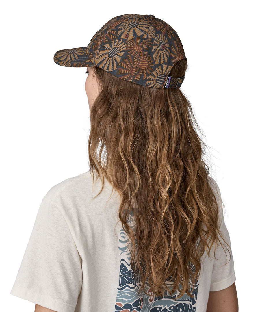 A woman wearing a Patagonia Adult P-6 Label Trad Cap in a Sun Wave design stood in front of a plain background. The woman is facing away from the camera showing the back of the cap. 