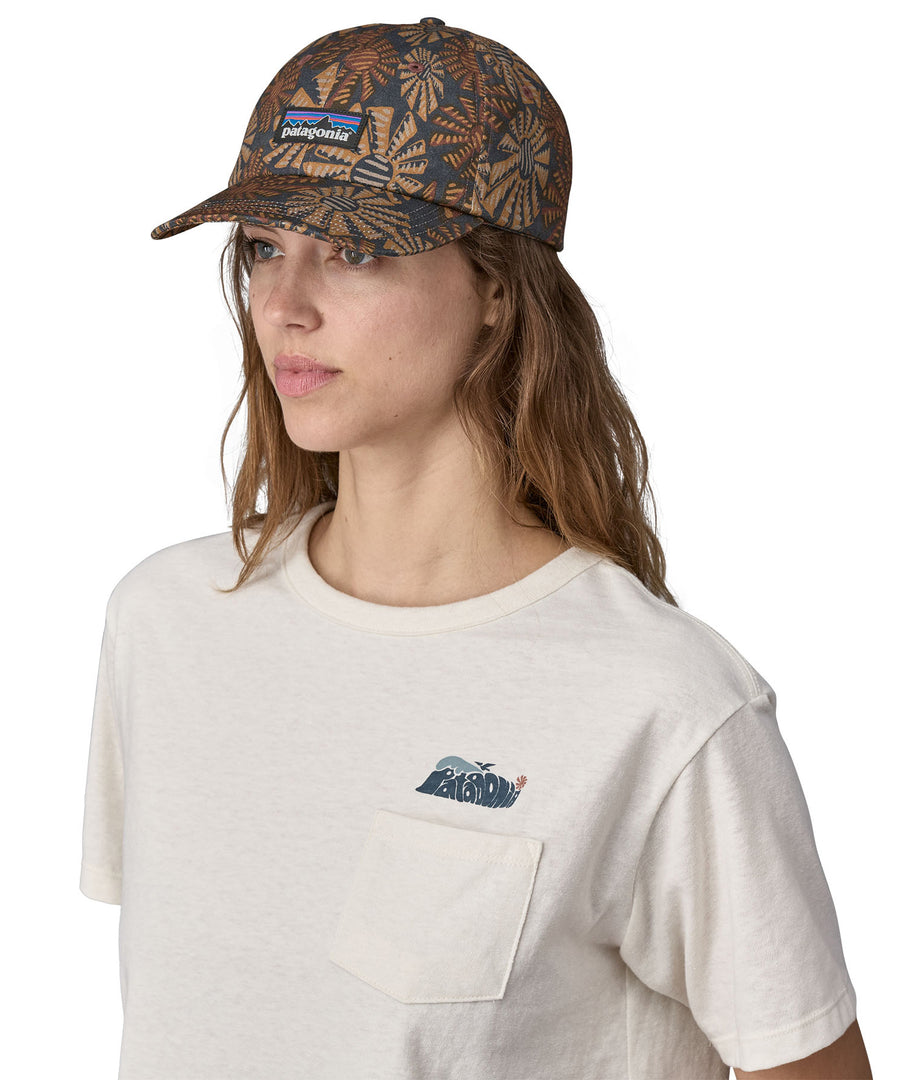 A woman wearing a Patagonia Adult P-6 Label Trad Cap in a Sun Wave design stood in front of a plain background.