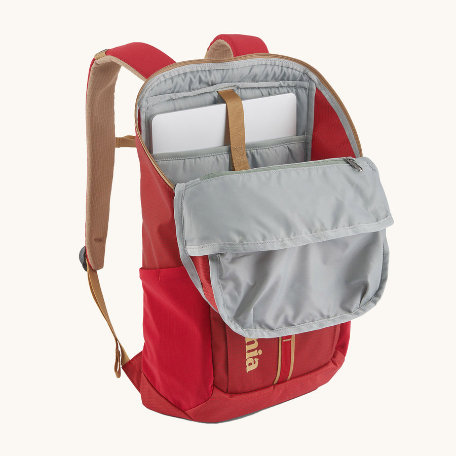 Patagonia Recycled Black Hole Backpack 25L in Touring Red with a map in the front zipper pocket and small essentials in the lid pocket on a cream background