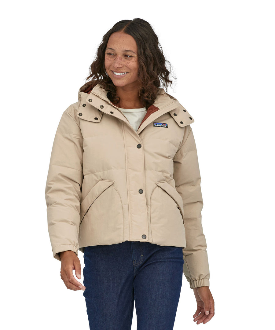 A woman with dark coloured shoulder length wavy hair wearing the Patagonia Women's Downdrift Jacket in Oar Tan