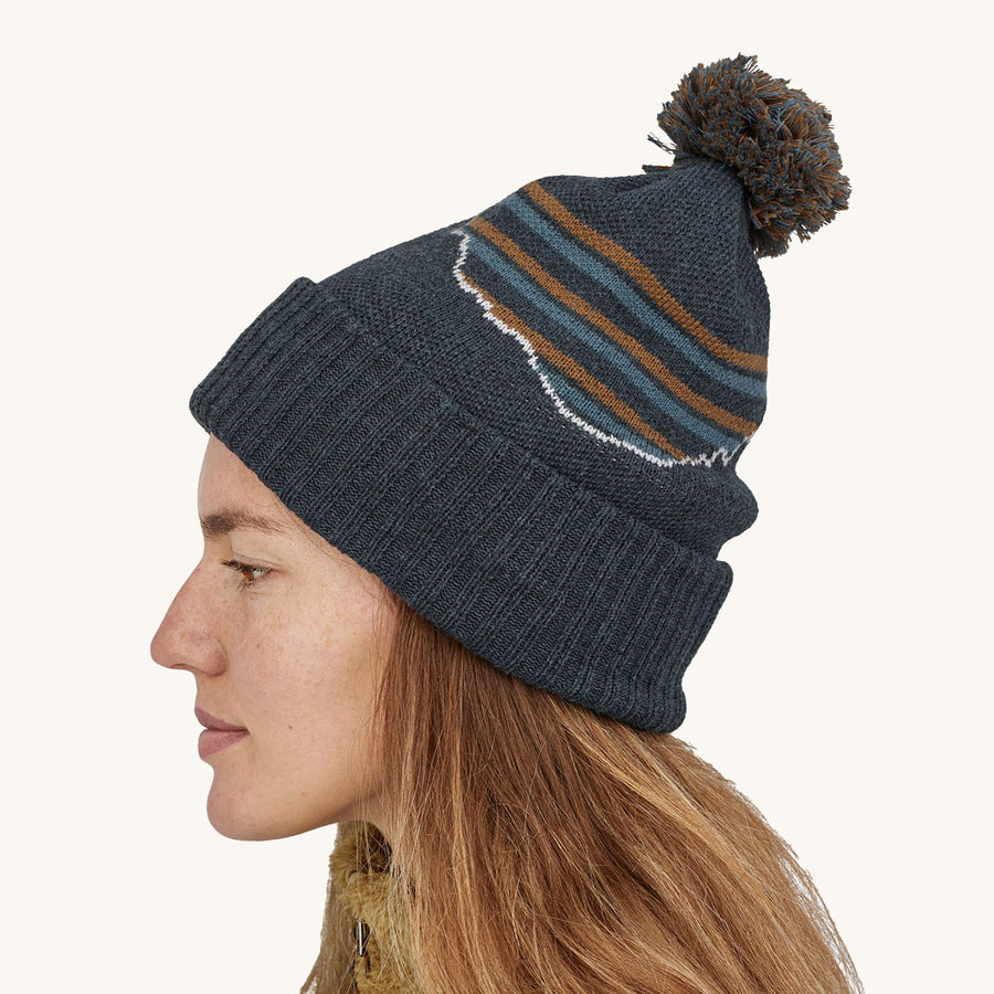 Patagonia Powder Town Beanie Bobble Hat - Fitz Roy Stripe Knit / Smolder Blue. A side profile of a woman wearing the hat against a plain background.