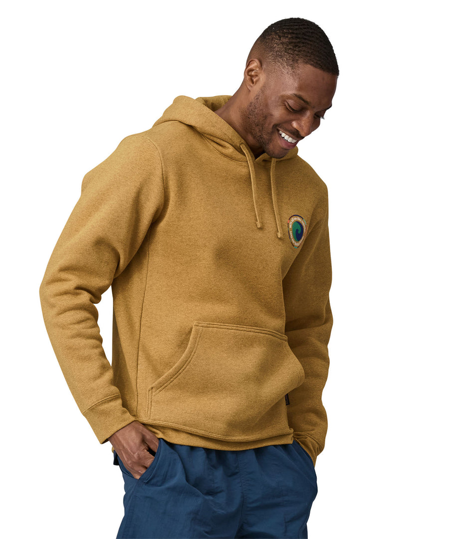 A man wearing a Patagonia Unity Fitz Uprisal Hoody in a yellow colour stood in front of a plain background.