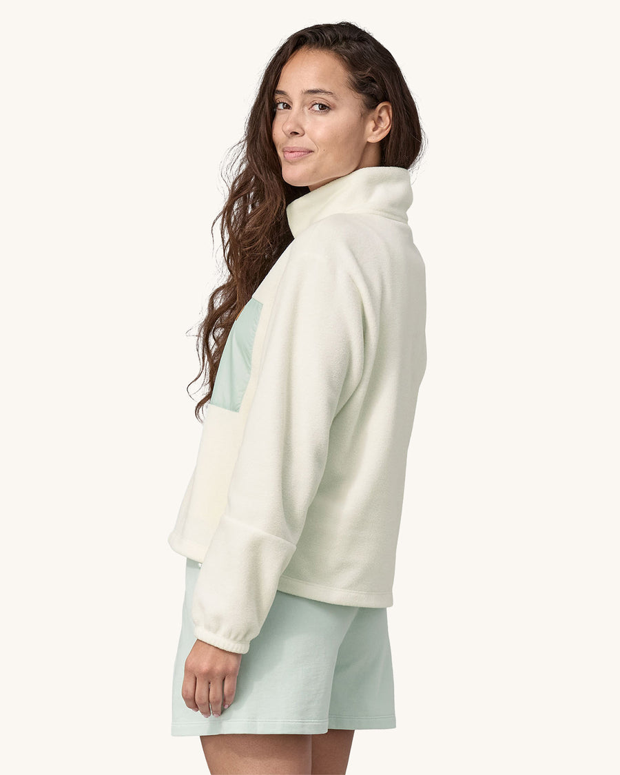 An adult wearing the Patagonia Women's Microdini 1/2 Zip Fleece Pullover - Birch White with a light blue pocket and zips