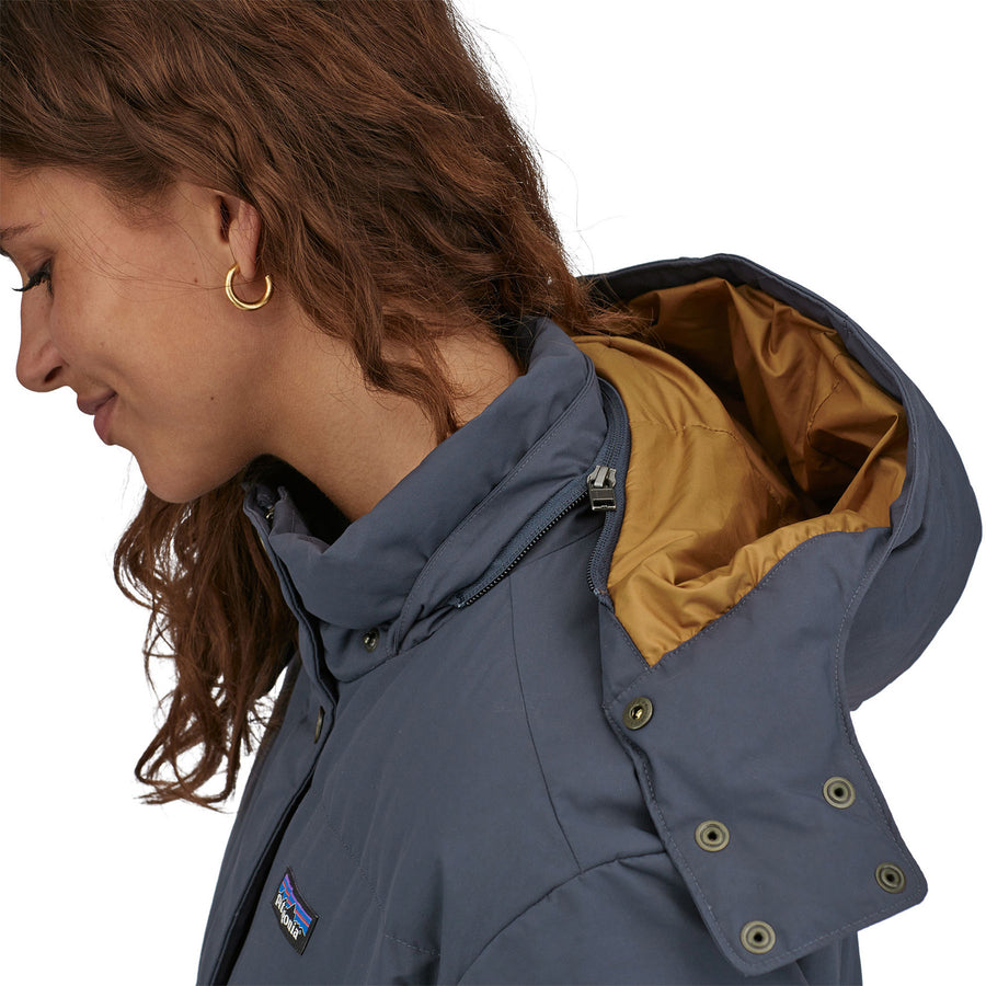 A close up of a person wearing the Patagonia Women's Downdrift Parka in Pine Smolder Blue showing the hood down and the zip that can be used to detatch the hood