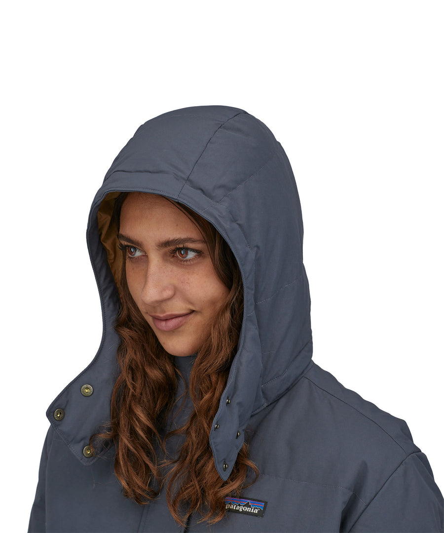 A close up of a person wearing the Patagonia Women's Downdrift Parka in Pine Smolder Blue showing the hood up 