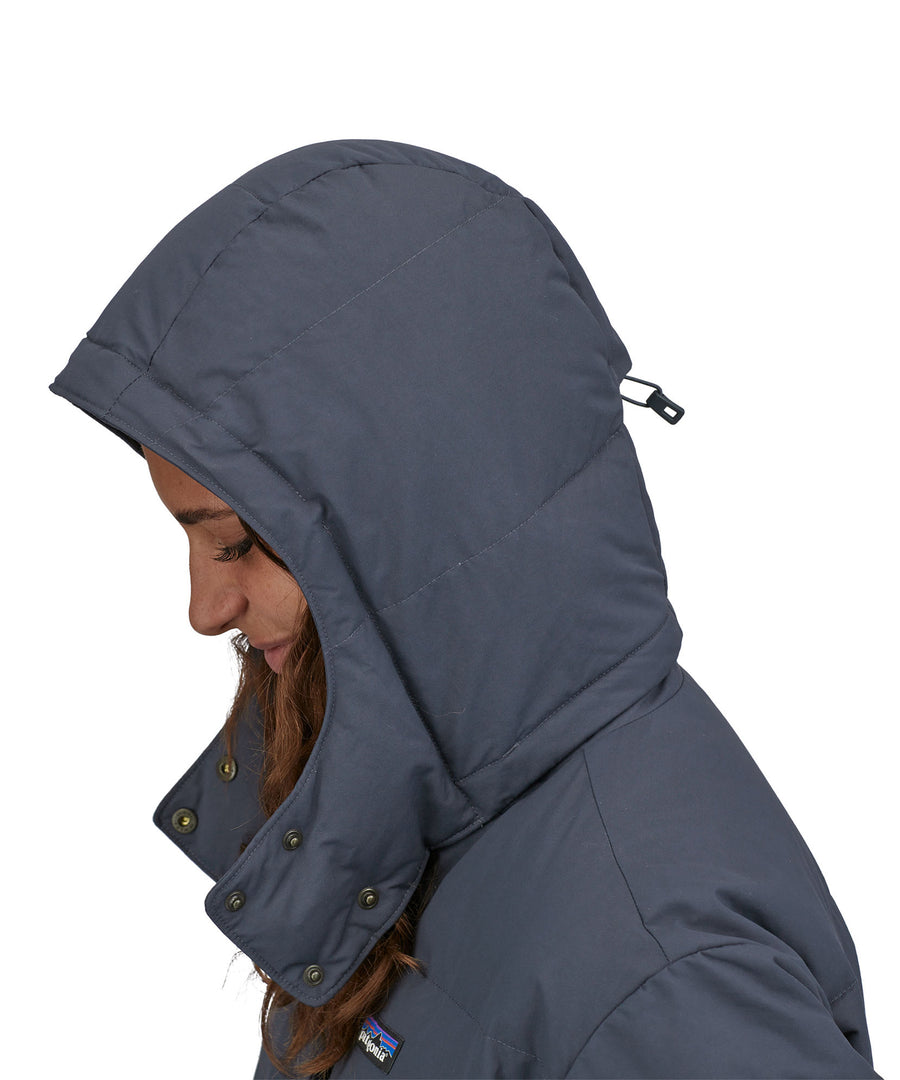 A side profile view close up of a person wearing the Patagonia Women's Downdrift Parka in Pine Smolder Blue showing the hood up 