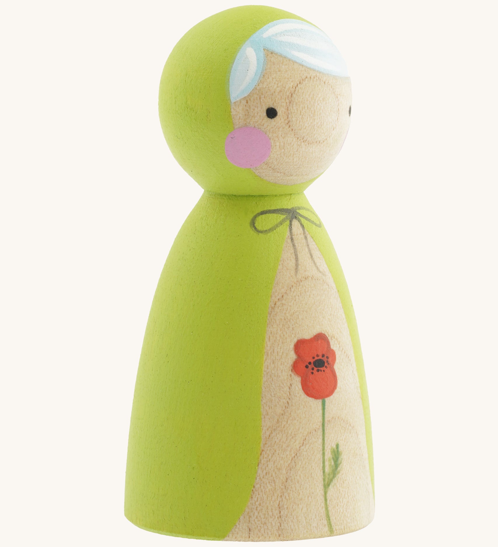 A side photo of the wooden handmade Peepul peg doll wearing a light green cape with a red poppy painted on the front on cream background.