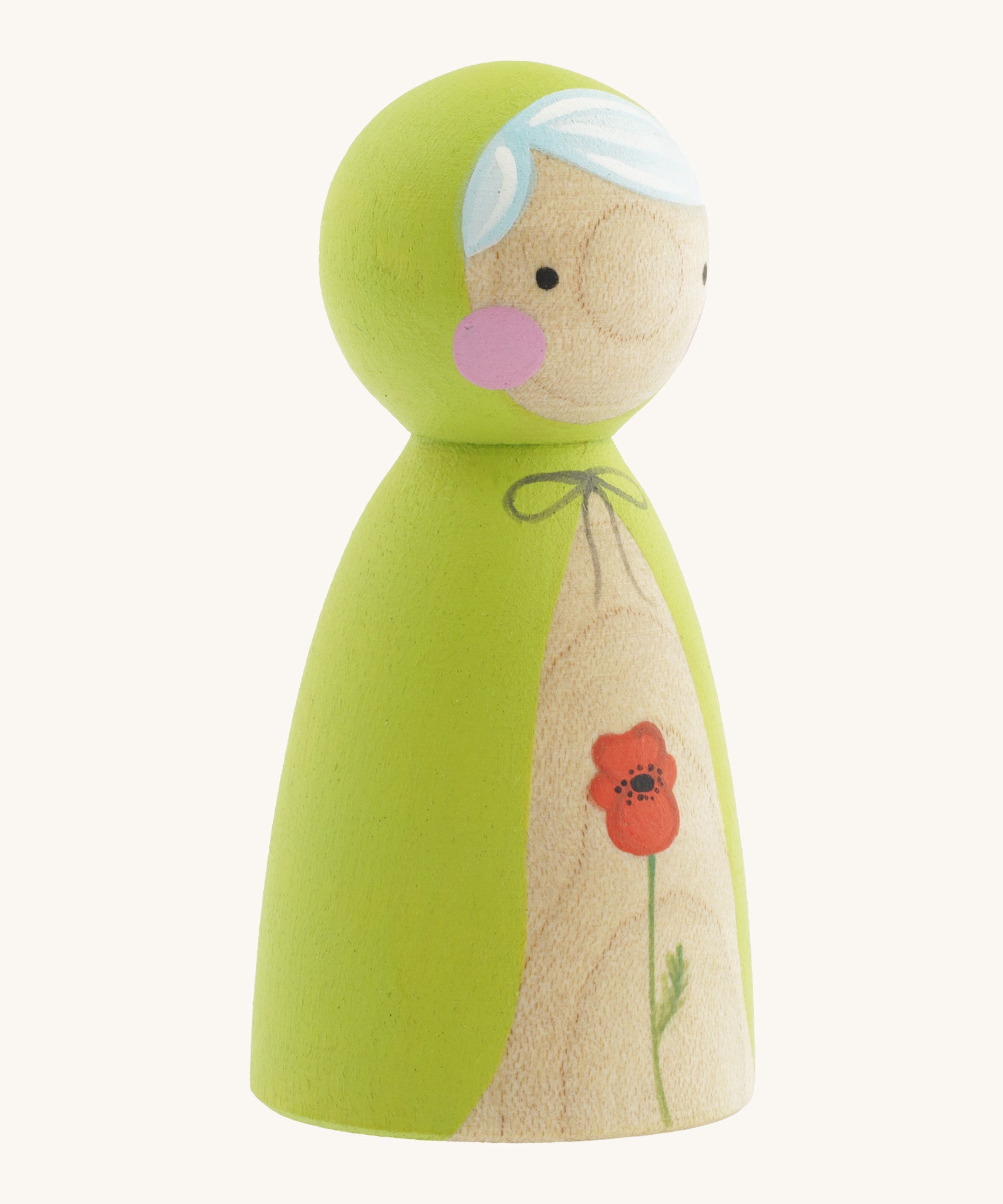 A side photo of the wooden handmade Peepul peg doll wearing a light green cape with a red poppy painted on the front on cream background.