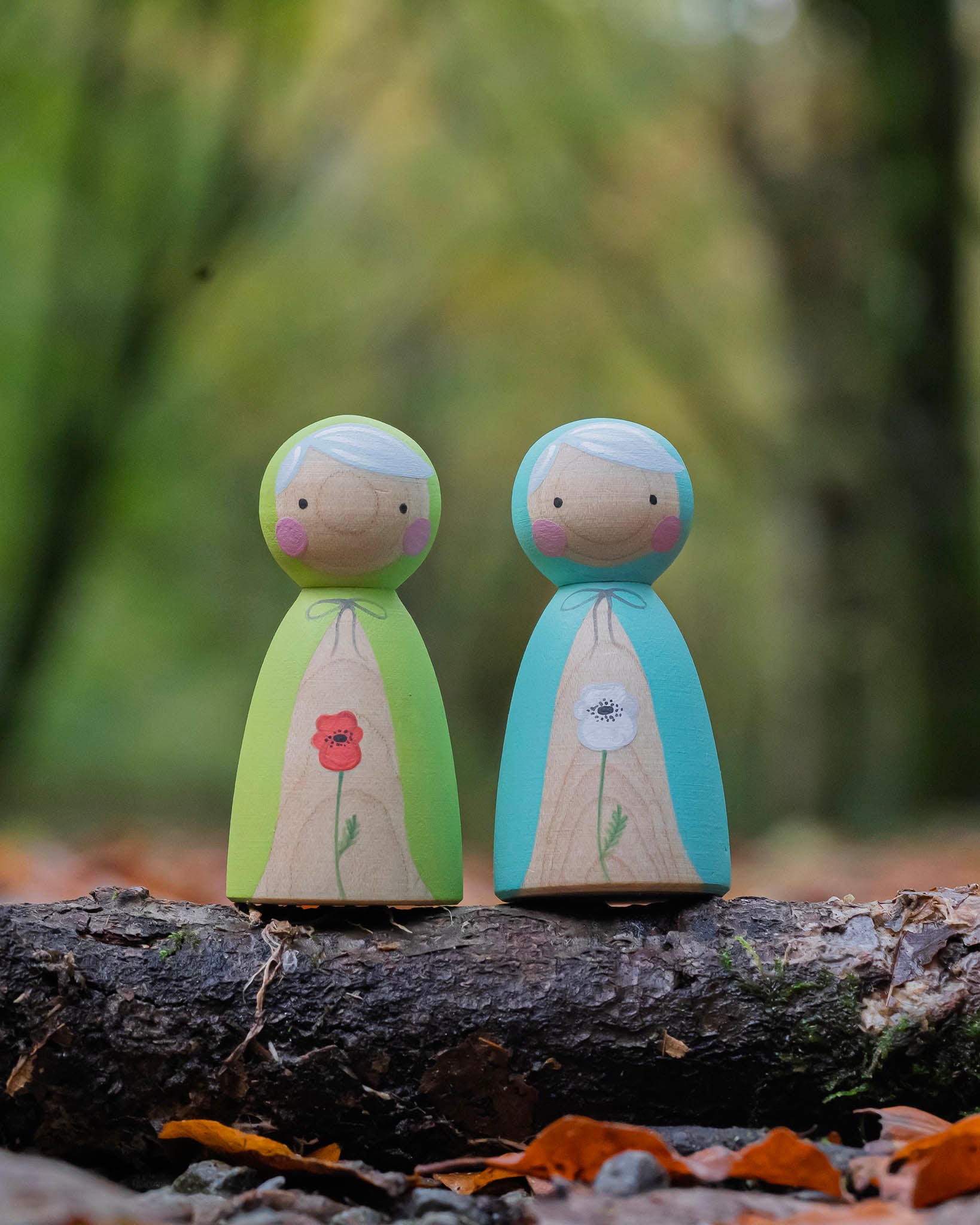 two hand painted peg dolls, one with a white poppy painted on its front, the other with a red poppy