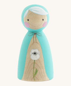 A wooden handmade Peepul peg doll wearing a light blue cape with a white poppy painted on the front on cream background.