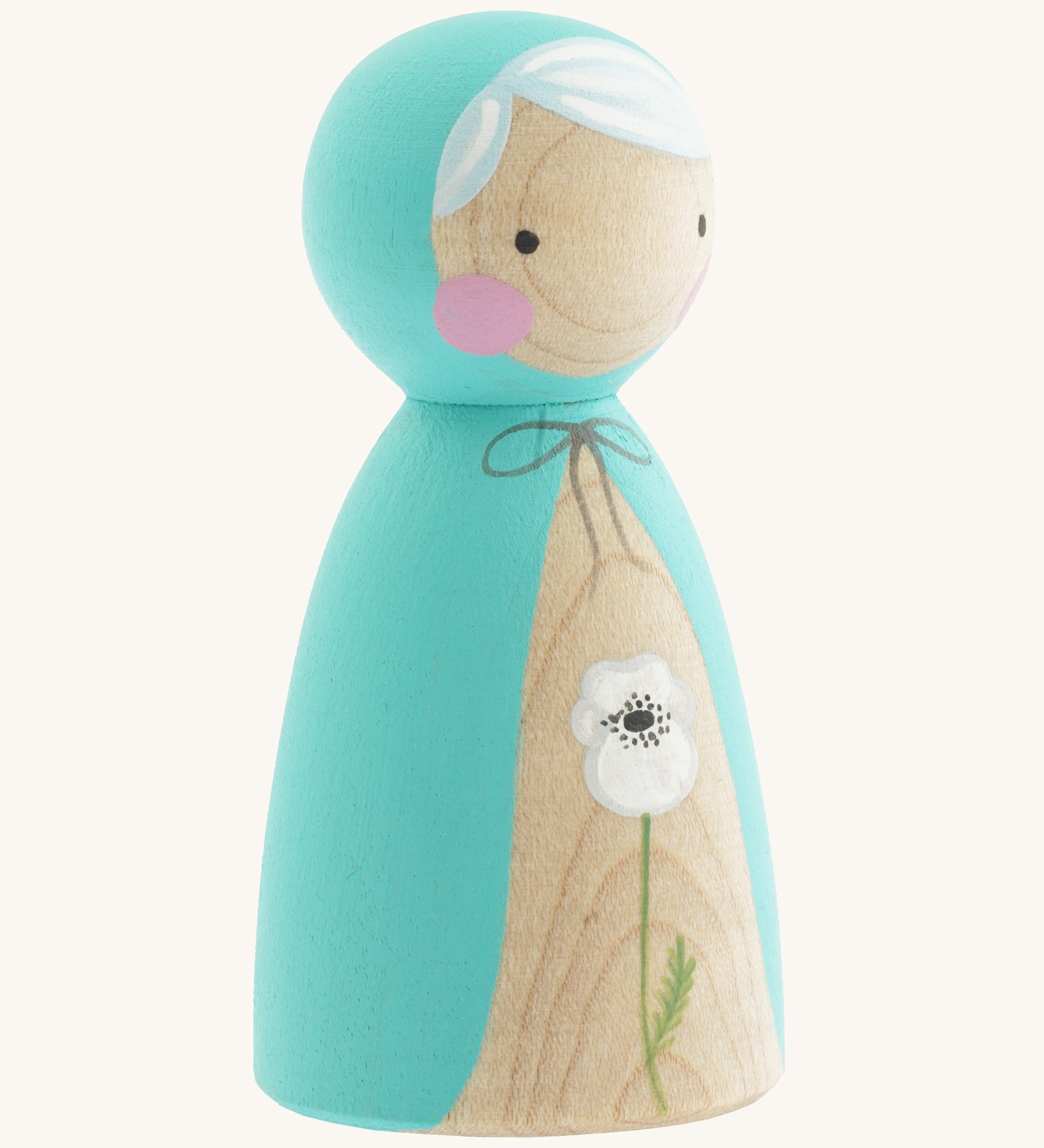 A side photo of the wooden handmade Peepul peg doll wearing a light blue cape with a white poppy painted on the front on cream background.