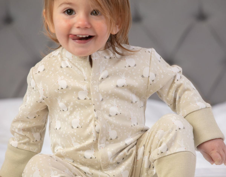 close up of top part of toddler wearing cotton tail footless onesie with a white rabbit all-over print on pale cream and stretchy cream cuffs from piccalilly