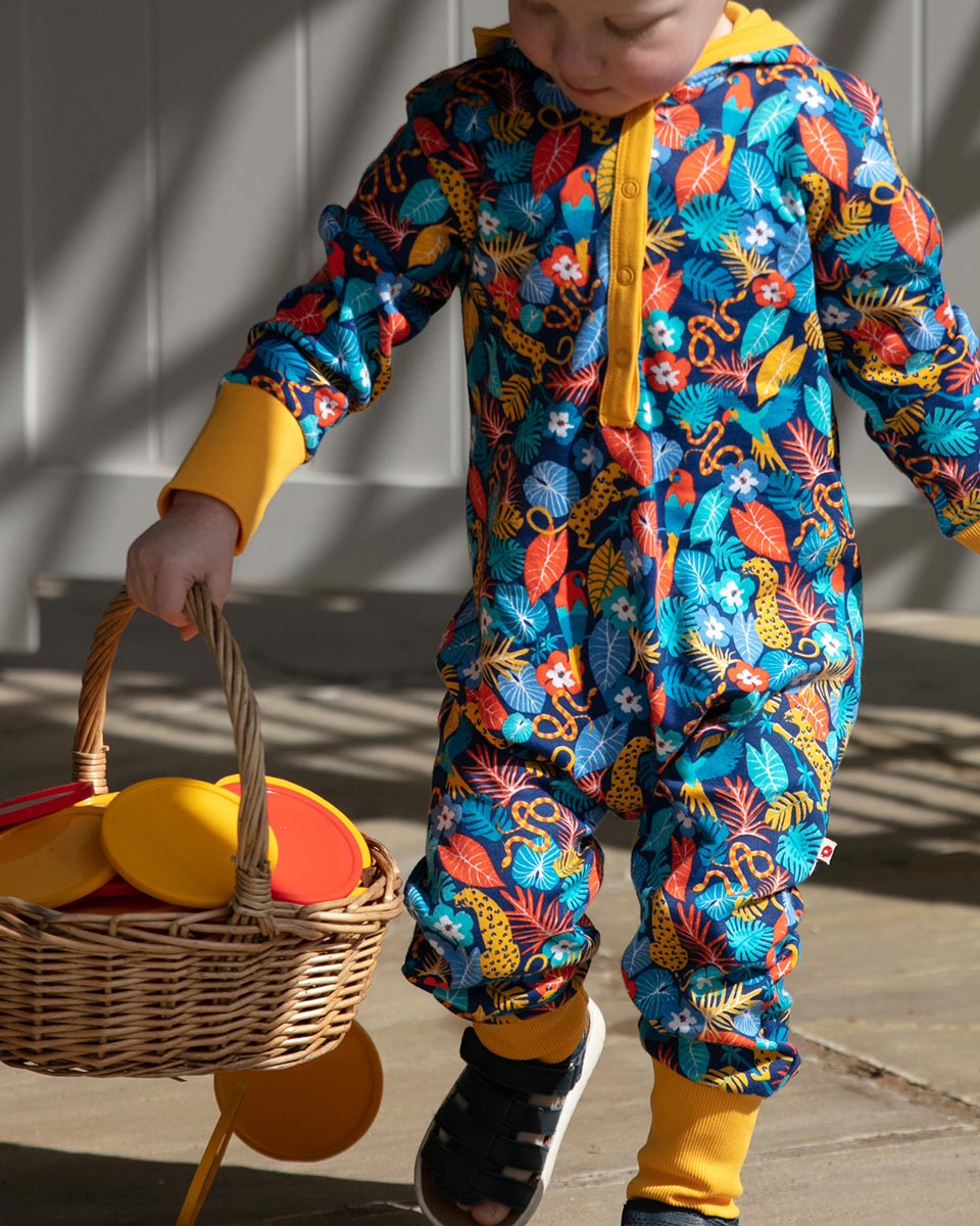 Young boy sat on some stone steps wearing the multicoloured Piccalilly organic cotton hooded playsuit