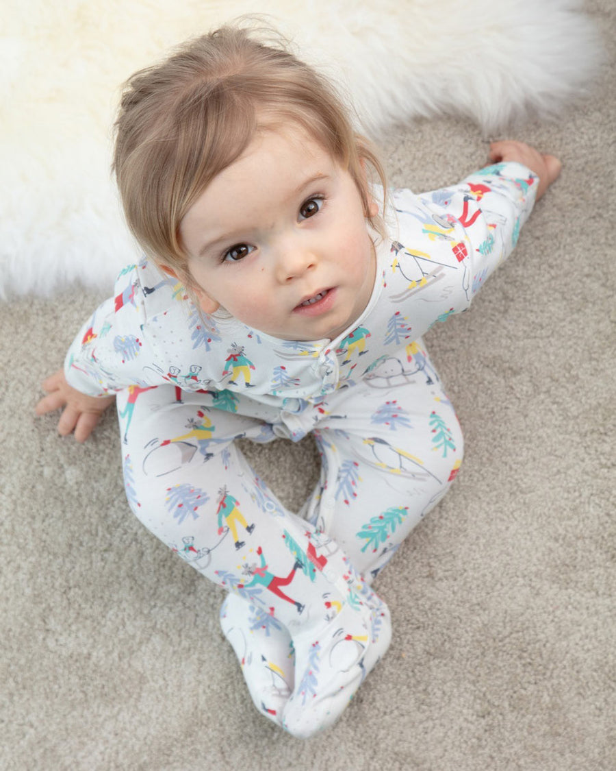 Girl sat on a grey floor looking up wearing the Piccalily organic cotton nightwear suit in the winter wonderland print