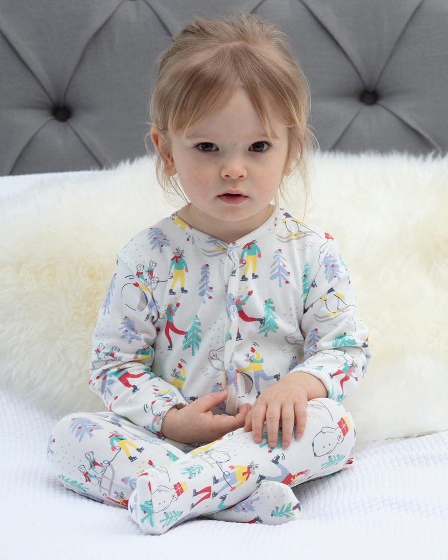 Girl sat on a white bed wearing the Piccalily organic cotton winter wonderland footed play suit 