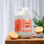 Bio-D Pink Grapefruit scented natural Washing Up Liquid in a 5 litre refill bottle on a wooden table with cut grapefruit