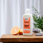 Bio-D vegan friendly Pink Grapefruit scented Washing Up Liquid in a 750ml bottle on a wooden table with cut grapefruits