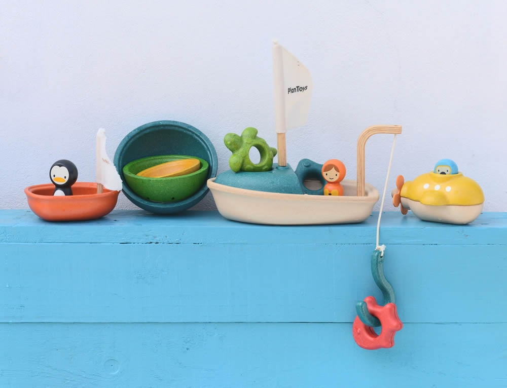 A collection of PlanToys wooden bath toys on a blue painted surface. 