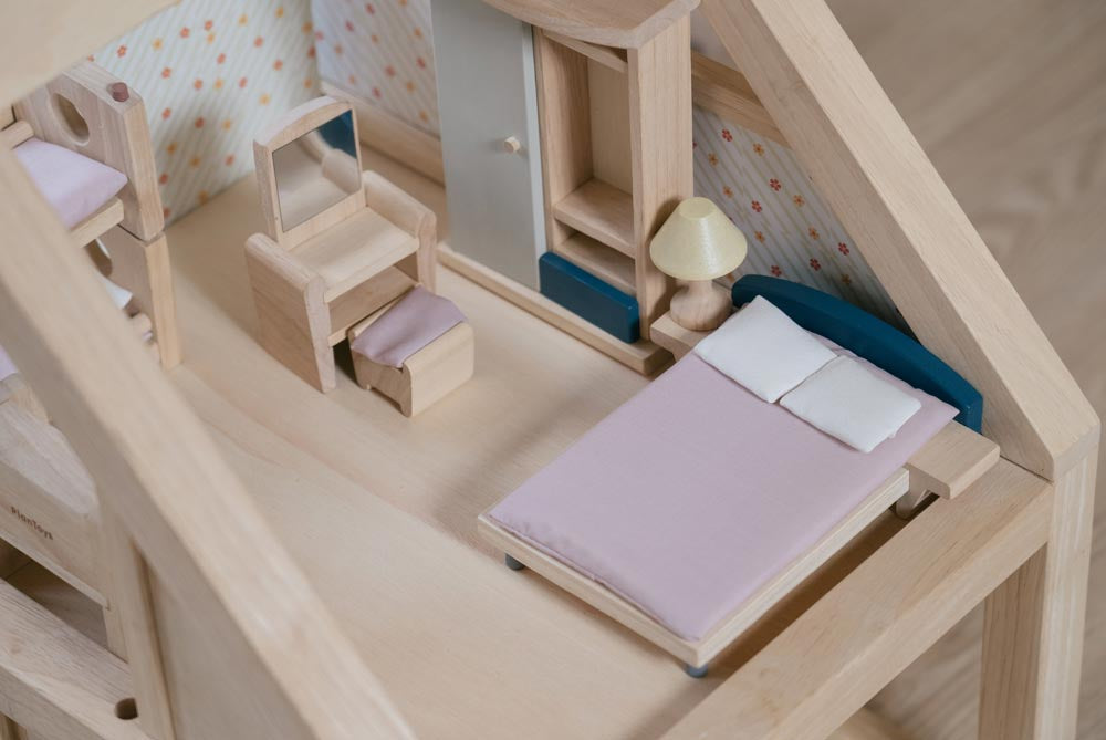 A close up of the bed from the PlanToys Bedroom Dolls House Furniture set placed in a room in a wooden dolls house. 