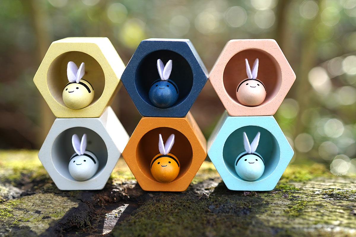 The PlanToys Bee Hives in the Orchard colour way placed on a moss covered log outdoors. 