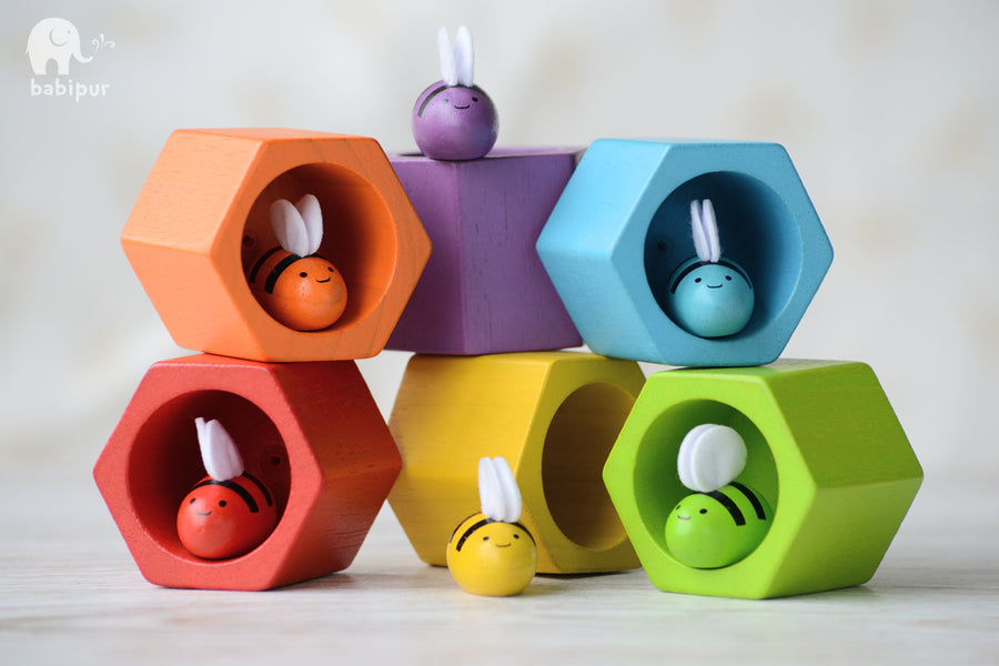 colourful wooden bees in their corresponding coloured hexagonal pot. White background.