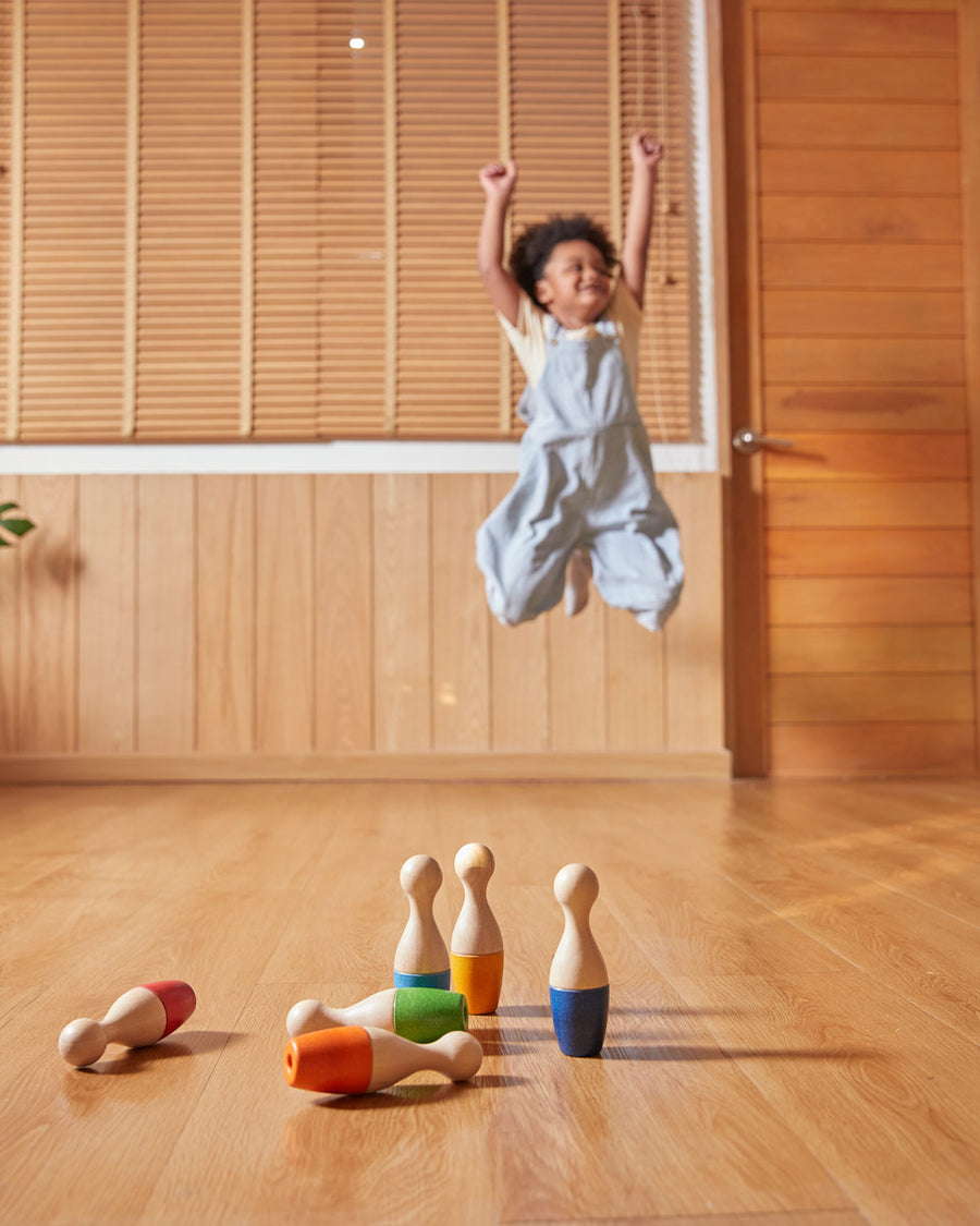 Close up of the PlanToys plastic-free bowling pins scattered on a wooden floor in front of a child