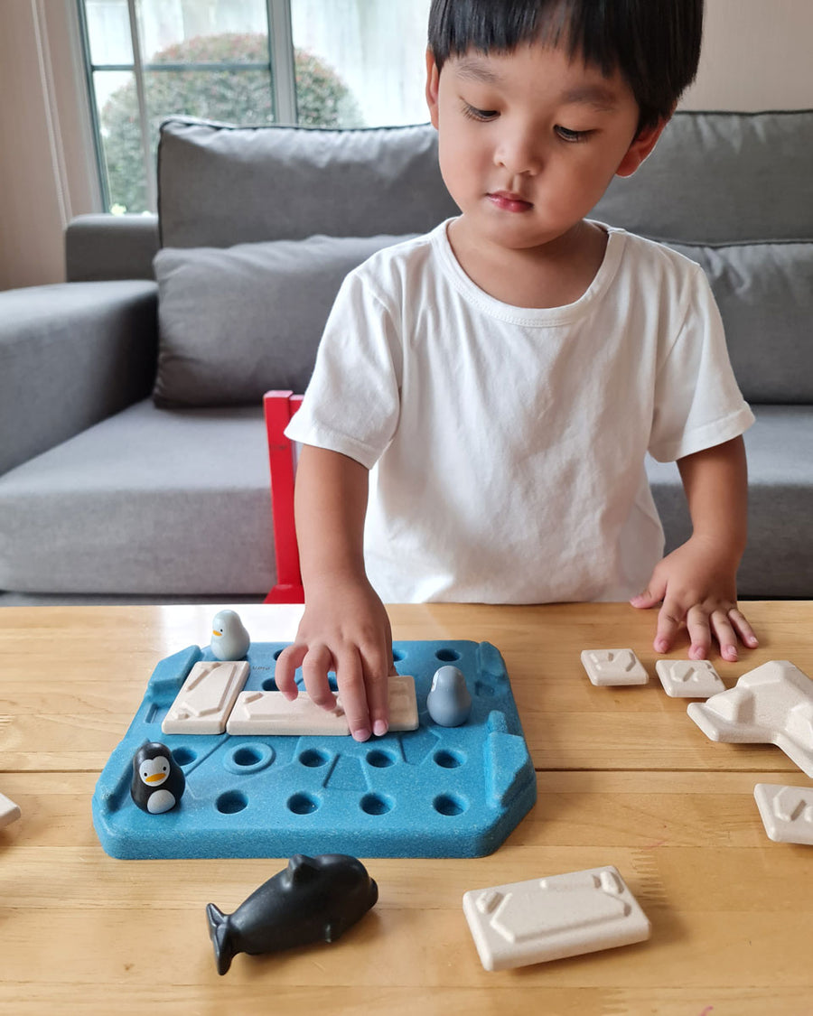 Boy playing with the Plan Toys eco-friendly penguin themed family game on a wooden table