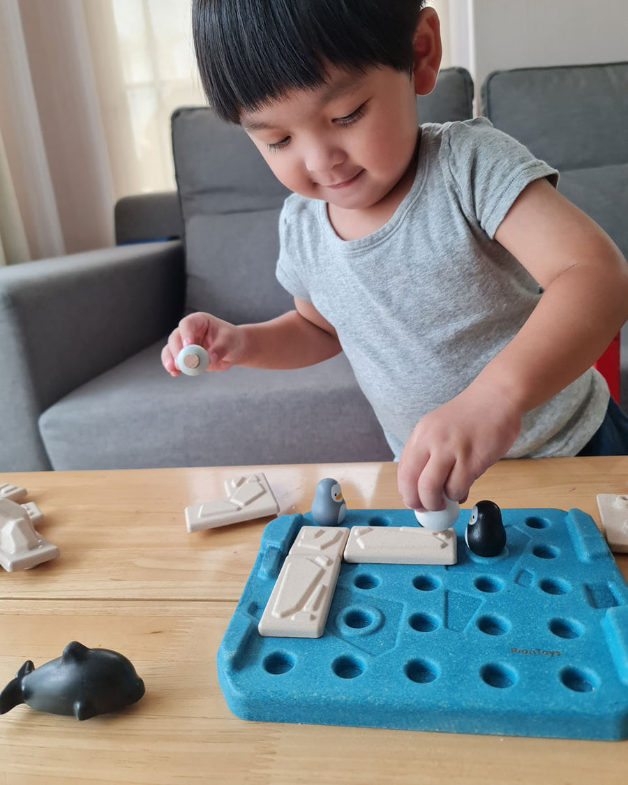 Boy moving the pieces of the Plan Toys plastic free finding penguin family board game on a light wooden table