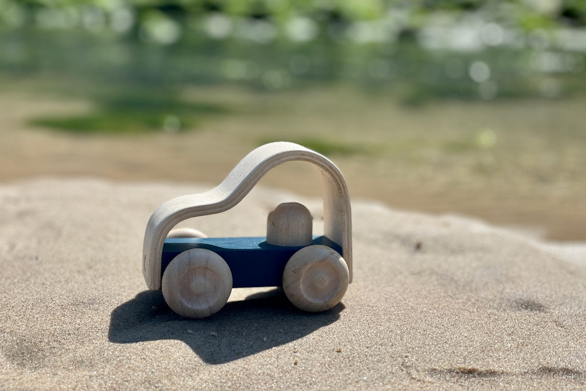 Close up of the Plan Toys kids eco-friendly vroom lorry toy on some sand in front of some green sea water