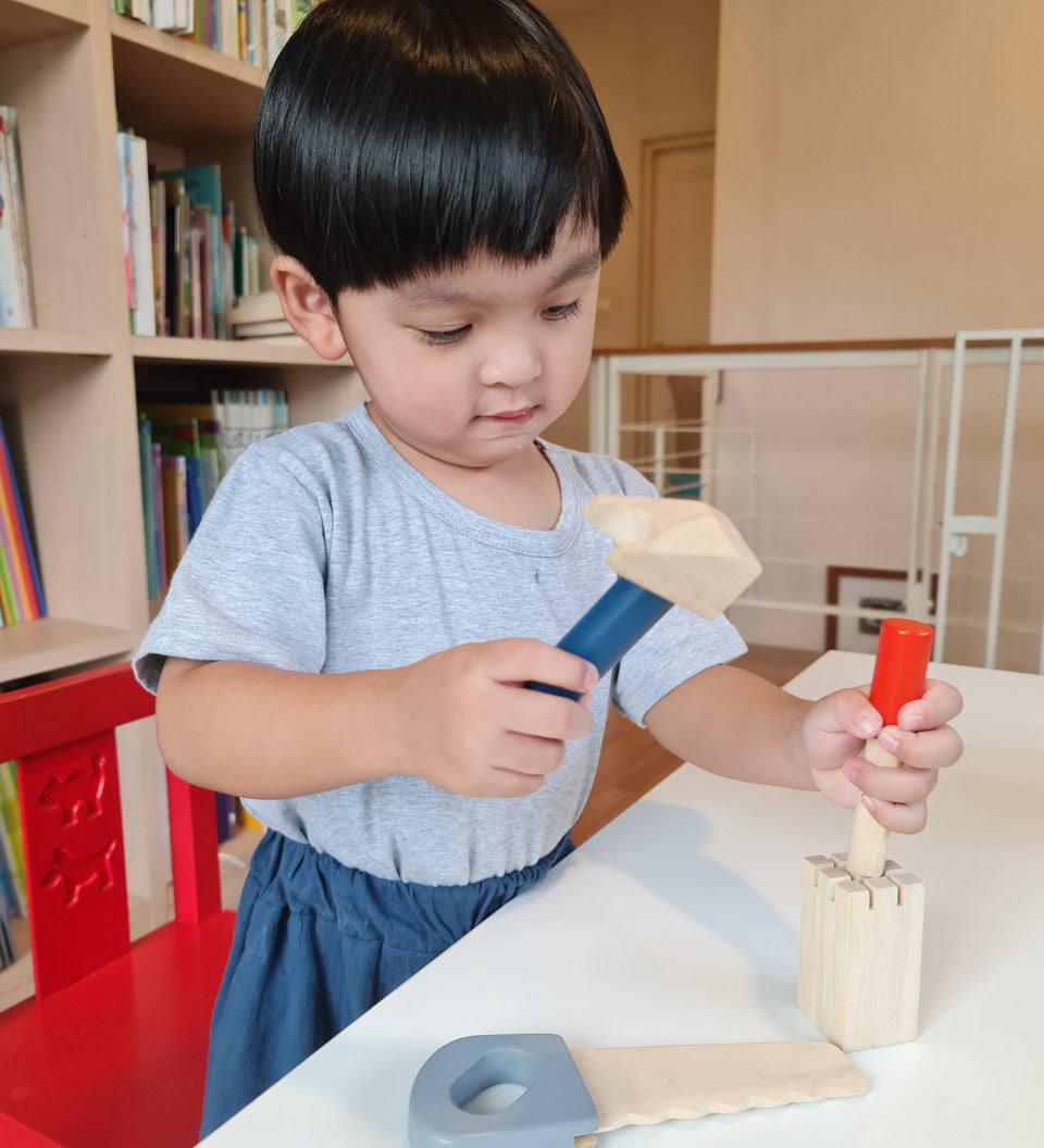 Boy stood at a table playing with the Plan Toys wooden chisel and mallet toy