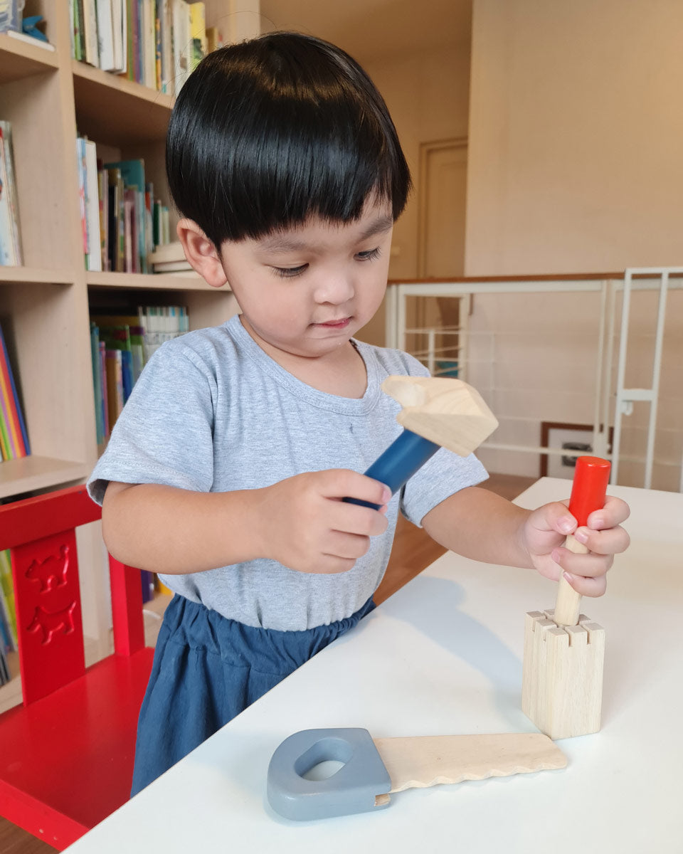 Boy stood at a table playing with the Plan Toys wooden chisel and mallet toy