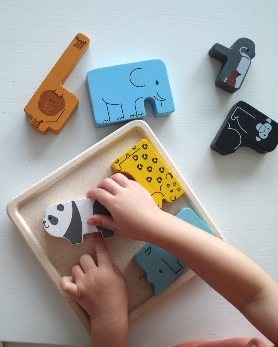 Close up of a childs hands moving the pieces from the Plan Toys plastic free animal puzzle game on a white table